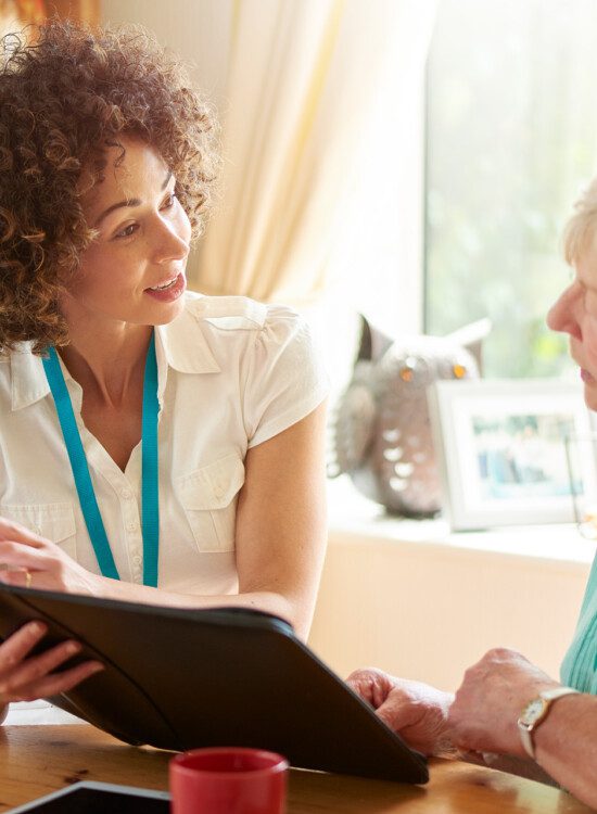 a care worker or medical professional or housing officer makes a house call to a senior client at her home . She is discussing the senior woman’s options on her digital tablet.