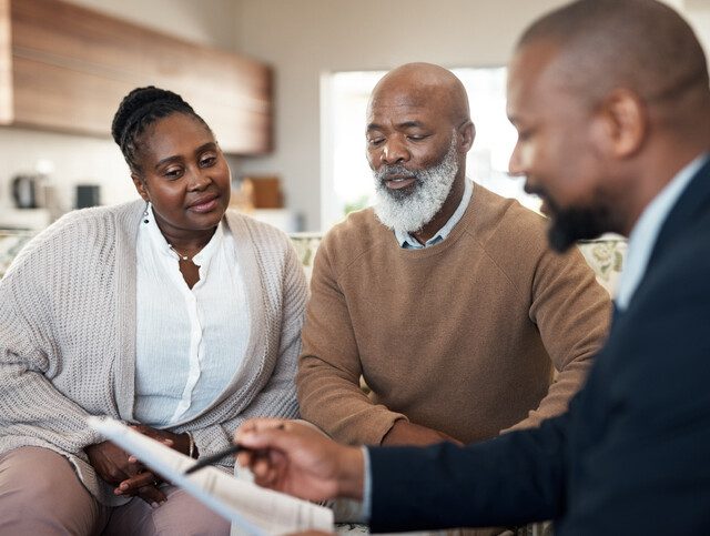 Mature black couple discussing their finances and planning retirement with an advisor at home. Senior husband and wife getting help with paperwork, investments or savings by a trusted agent