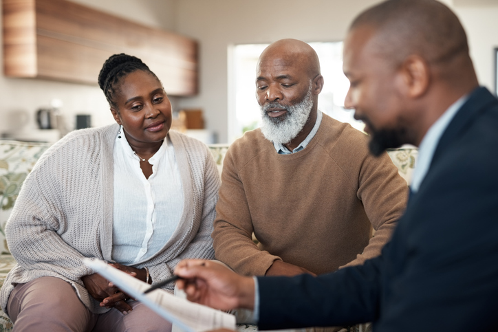 Mature black couple discussing their finances and planning retirement with an advisor at home. Senior husband and wife getting help with paperwork, investments or savings by a trusted agent