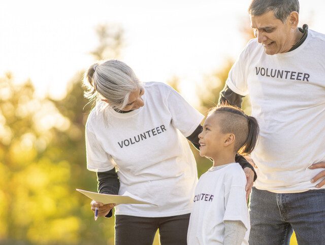 A young boy and his grandparents assemble outside together on a sunny day as they volunteer their time in the community.